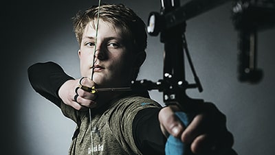 An archer holding a compound bow with it drawn.